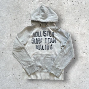 Hollister Surf Team Malibu Hoodie - Hollister Surf Hoodie : Grå : Skick 9/10 endast en liten fläck på bild 5 : Hoodien har en sliten design och inte pga användning : Size M passar M/S : Väldigt sällsynt då den inte säljs längre : Köptes second hand dvs inget kvitto : Kom privat för mer bilder och mått etc.