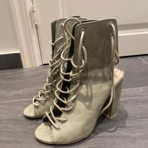 Gröna mocka stövletter med snörning - Snygga gröna stövletter i mocka med chunky klack och öppen tå. Skorna har cool snörning hela vägen upp och en modern, edgy vibe. Perfekta för dig som vill sticka ut med din stil och gillar statement-detaljer. Storlek 37.