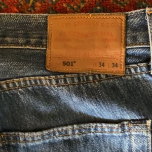 Levi's 501 blå jeans W34 L34 - Klassiska blå Levi's 501 jeans med rak passform och femficksdesign. Jeansen har en ikonisk läderpatch bak i midjan och är tillverkade i slitstarkt denim. Perfekta för dig som gillar tidlös stil och vill ha ett par riktigt schyssta jeans.