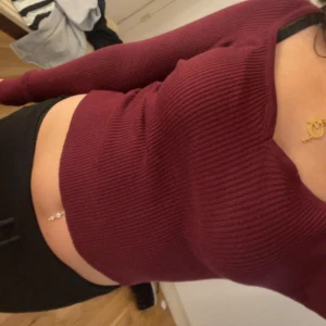 Vinröd ribbad croppad långärmad topp - Säljer en vinröd långärmad topp med croppad passform och ribbad struktur. Toppen har en snygg v-ringning och sitter tight mot kroppen. Perfekt att styla med jeans eller kjol för en trendig look.