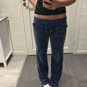 Blå byxor från Juicy Couture - Mysiga blå mjukisbyxor från Juicy Couture i velour med bred midja, snörning och fickor både fram och bak. Byxorna har broderad JC-logga och raka ben för en chill och snygg look.