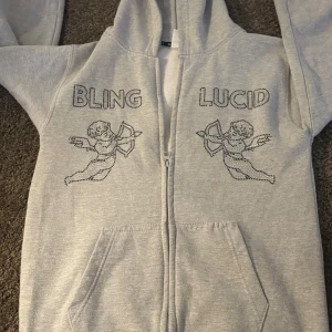 Bling Lucid kofta  - Grå zip-hoodie från Bling Lucid med snygga änglar och BLING LUCID” på bröstet 📏 Storlek: XL (12/13 år, 👕 Material: 75% bomull / 25% polyester – supermjuk och bekväm