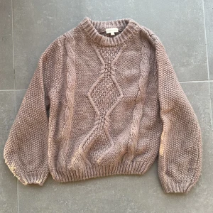 Rosa stickad tröja  - Säljer en rosa stickad tröja från Polpdelux med snyggt flätmönster. Tröjan har rund halsringning och är långärmad, perfekt för kyliga dagar. Den är mjuk och skön. 