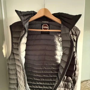 Colmer väst S  - Snygg grå dunväst från Colmar med horisontella sömmar och hög krage. Västen har två fickor med dragkedja och en diskret logga på bröstet. Perfekt att slänga över en hoodie eller tröja när det är kyligt ute.