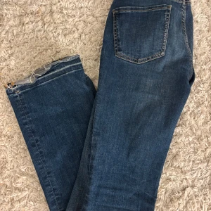 Blå jeans från Zara, storlek 34 - Snygga blå jeans från Zara i klassisk femficksmodell med raka ben och rå kant nedtill. Jeansen har en mörk tvätt och kontrastsömmar, vilket ger en cool och avslappnad vibe. Perfekt för dig som gillar enkel och stilren denim.