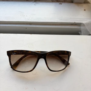 Bruna Ray-Ban Wayfarer solglasögon - Snygga solglasögon från Ray-Ban i klassisk Wayfarer-modell med brunmelerat skal och stora, fyrkantiga bågar. Glasen är tonade i brunt och bågarna har en cool sköldpaddsmönstrad look. Perfekta för att lyfta din stil i solen.