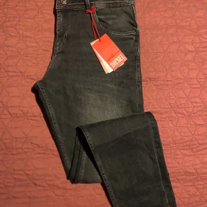 Svarta Diesel jeans med röda detaljer W33 L40 - Snygga svarta jeans från Diesel med röda sömmar och klassisk femficksdesign. Jeansen har en diskret tvättad look och logotyp på myntfickan. Perfekta för dig som gillar en stilren men edgy vibe.