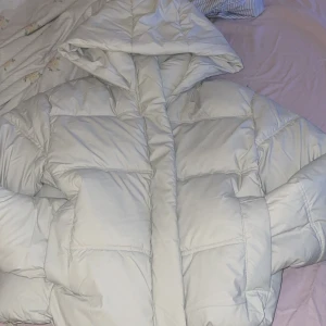 Vit pufferjacka HELT NY! - Säljer en riktigt snygg vit pufferjacka från FBSISTER. Jackan har en stor huva, breda kanaler och stängs med dragkedja. Perfekt för kalla dagar när du vill hålla dig varm och ändå se stilren ut. Jackan är vadderad och har en clean look. Säljer pågrund av att jag köpte fel storlek