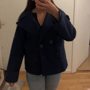Mörkblå skepparkavaj med stora slag - Säljer en klassisk mörkblå skepparkavaj med dubbelknäppning och stora slag. Jackan har långa ärmar och bred passform, perfekt för dig som gillar en tidlös och stilren look. Snygg till både jeans och kjol.