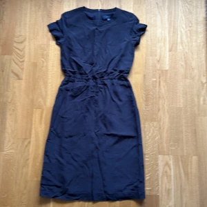 Marinblå klänning från Gant - Snygg marinblå klänning från Gant i klassisk modell med korta ärmar och rund halsringning. Klänningen har markerad midja med resår och dragkedja bak. Perfekt för dig som gillar stilrena och tidlösa plagg.