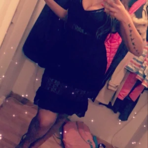 Svart spetsklänning med volang - Supersnygg svart kortklänning från Love & Divine i spets med prickigt mönster. Klänningen har v-ringning, volangdetaljer vid axlarna och är ärmlös. Genomskinliga partier i spets ger en extra touch. Perfekt för dig som vill sticka ut med en elegant look.