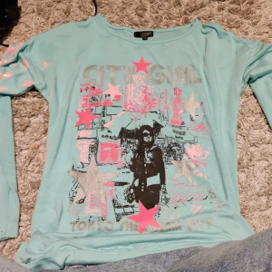 Turkos långärmad tröja med tryck - Turkos långärmad tröja från KappAhl med coolt tryck på framsidan som visar en stadsscen och texten 'CITY GIRL' samt 'TOKYO THE DREAM CITY'. Trycket har silver- och rosa stjärnor. Mjuk bomullskänsla och rund hals. Säljs inte längre i butik