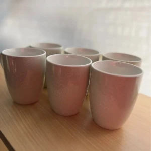 6 kaffemuggar  - Bilderna visar sex vita porslinsmuggar med subtilt mönster. Muggarna ser ut att vara i gott skick utan synliga sprickor eller nagg. Perfekt för kaffe eller te, stilrena och passar i de flesta kök. 