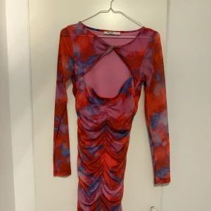 Färgstark meshklänning från NA-KD - Säljer en supercool långärmad meshklänning från NA-KD i storlek S. Klänningen har ett rött och lila abstrakt mönster, snygg cut-out framtill och rynkade detaljer längs hela framsidan. Tight passform och stretchigt material som sitter perfekt.