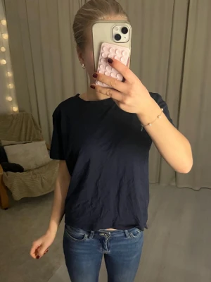 Mörkblå basic t-shirt - En enkel och stilren mörkblå t-shirt med korta ärmar och rund halsringning. Modellen är rak och lite loose, perfekt till jeans eller shorts. T-shirten är i mjukt material, troligtvis bomull, och passar dig som gillar en clean och avslappnad look.