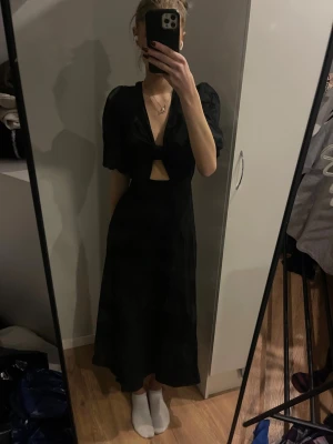 Svart långklänning från H&M med cut out - Säljer en svart långklänning från H&M i storlek 34. Klänningen har puffiga korta ärmar, v-ringning och snygga cut out-detaljer både fram och bak. Materialet är skönt, klänningen är helt ny och aldrig använd!