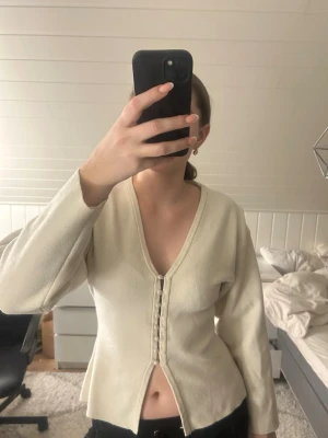 Beige tröja  med knappar från Gina Tricot - Säljer en beige tröja Gina Tricot i storlek M. Koftan har v-ringning, långa ärmar och dekorativa tygklädda knappar framtill. Materialet känns mjukt och tröjan har en figurnära passform med liten slits nedtill. Den har en del nopprar på sig, försökte ta kort på de. Enda defekten jag kan se, man är flitigt använt!🥰