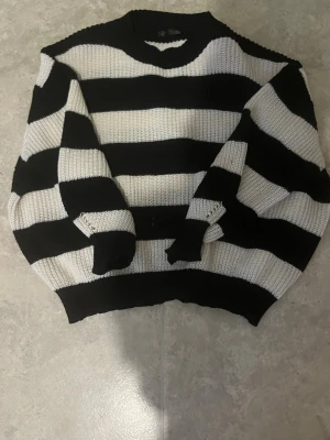 Svartvit randig stickad tröja - Säljer en stickad tröja med breda svarta och vita ränder. Tröjan har rund halsringning och långa ärmar med ribbade muddar. Perfekt för dig som gillar en chill och trendig look med lite oversized känsla.