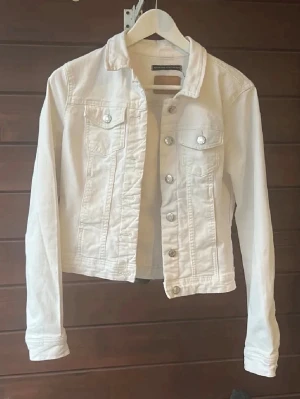 Vit jeansjacka  - Snygg vit jeansjacka från Only med klassisk krage och silverfärgade knappar framtill. Jackan har två bröstfickor med lock och långa ärmar med knapp vid ärmslut. Perfekt att slänga över en t-shirt för en fräsch look.