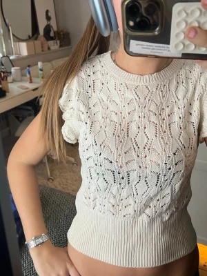 Vit stickad blus från Lindex - Supersöt vit stickad blus från Lindex i storlek S. Toppen har ett genombrutet mönster, volangärmar och bred ribbad midja. Perfekt till jeans eller kjol för en fräsch look. Materialet är mjukt och luftigt, perfekt för vår och sommar.