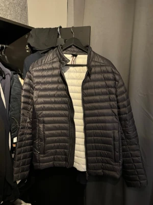 Svart pufferjacka från Colmar - Säljer en svart pufferjacka från Colmar Originals med diskret logga på ärmen. Jackan har horisontella quiltade sömmar, dragkedja framtill och ståkrage. Insidan är ljusgrå och materialet är lätt och smidigt, perfekt för kyliga dagar.