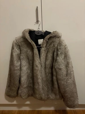 Grå pälsjacka med huva från Zara Woman - Mjuk fluffig grå pälsjacka från Zara Woman med huva. Jackan har en loose passform och är helfodrad med svart tyg på insidan. Perfekt för kalla dagar och har en riktigt mysig vibe. Jackan är i storlek M och har långa ärmar.