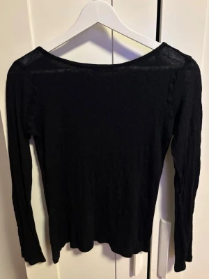 Svart långärmad topp i tunnt tyg - Enkel svart långärmad topp i tunnt tyg. Modellen har rundad halsringning och sitter figurnära utan att vara för tight. Står inte storlek men skulle säga S/M. Tröjan är lite genomskinlig