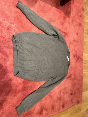 Grå stickad tröja Mauro Grifoni - Snygg grå stickad tröja från Mauro Grifoni, tillverkad i Italien. Tröjan har rund hals, ribbade muddar vid ärmslut och nederkant samt långärmad passform. Perfekt för dig som gillar stilrena och klassiska plagg med en modern touch.