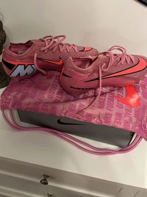 Nike vapor mercurial elite ag-PRO - Säljer ett par riktigt snygga rosa Nike fotbollsskor med svart och orange swoosh och coola detaljer på hälen. Skorna har snörning och är tillverkade i ett lätt syntetmaterial som ger bra känsla på planen. Perfekta för dig som vill sticka ut på matchen! Ord. Pris 3099 kr 