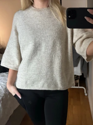 Beige stickad tröja med trekvartsärm - Mysig beige stickad tröja med rund hals och trekvartsärmar. Tröjan har en loose passform och är perfekt för lager på lager. Enkel och stilren design som passar till allt.