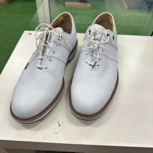 Vita golfskor DryJoys Premier Series - Snygga vita golfskor från DryJoys Premier Series med Ortholite-innersula. Skorna har snörning, rund tå och är tillverkade i skinn med detaljerad struktur. Yttersulan har kraftiga dobbar för bra grepp på golfbanan. Perfekta för dig som vill ha stil på greenen.
