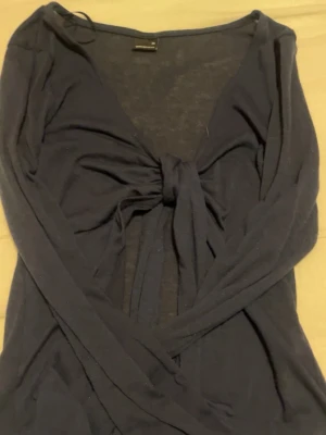 Svart blending topp med knyt - Snygg mörk blå topp från Gina Tricot med djup v-ringning och knyt framtill. Lång tröja med långa ganla ärmar och mjukt, tunt material som känns sopigt mot huden. Perfekt för att skapa en cool och avslappnad matta.