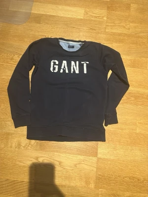 Svart sweatshirt från GANT - Cool svart sweatshirt från GANT med stort vitt tryck på bröstet. Klassisk rund halsringning och långa ärmar. Perfekt för dig som gillar enkel men snygg stil. Tillverkad i mjuk bomull för skön känsla hela dagen.