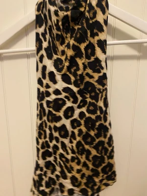 Leopardmönstrad polotopp  - Säljer en snygg polotopp i storlek S med leopardmönster i svart, beige och bruna toner. Toppen är ärmlös och har en hög krage som ger en cool vibe. Perfekt för dig som gillar att sticka ut med djurmönster och vill ha något trendigt i garderoben.