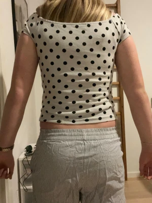 Prickig croppad topp från FB Sister - Säljer en vit croppad topp från FB Sister med svarta prickar. Toppen har korta ärmar och en bred, något offshoulder ringning. Materialet är mjukt och stretchigt, perfekt för en chill och trendig look.