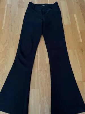Svarta bootcut byxor Gina Tricot XS - Säljer ett par svarta bootcut byxor från Gina Tricot i storlek XS. Byxorna har hög midja, två knappar och dragkedja framtill samt fickor med lock och knapp bak. Materialet är mjukt och stretchigt, perfekt för en snygg och bekväm look.