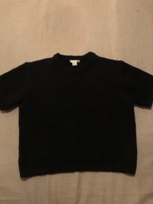 Svart stickad t-shirt från Gina Tricot - En svart stickad t-shirt från Gina Tricot i storlek 158/164 eller XS. Säljer tyvär denna fina tröjan för att jag behöver rensa i min garderob. Tröjan är knappast använd. Du betalar frakten!