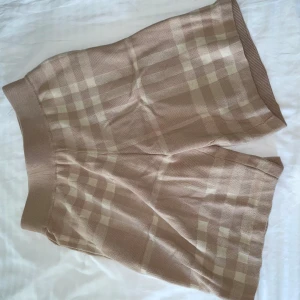Beige rutiga shorts från Burberry - Superfina beige shorts från Burberry med klassiskt rutigt mönster. De är stickade och har en bred, elastisk midja som sitter skönt. Perfekta för dig som gillar en chill men ändå stilren look. Passar till allt och är riktigt trendiga just nu.