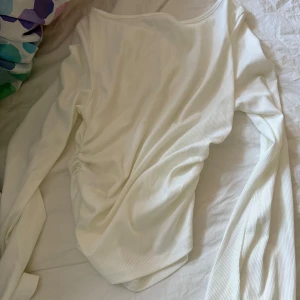 Ribbad långärmad topp i vitt och rosa - Två långärmade ribbade toppar i vitt och ljusrosa. Båda har en lätt rynkad detalj på sidan och är tillverkade i ett mjukt, stretchigt material. Perfekta att styla med jeans eller kjol för en enkel och snygg look.