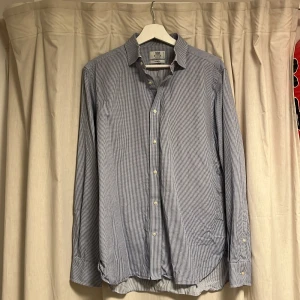 Rutig skjorta från Boggi Milano - Snygg rutig skjorta från Boggi Milano i vitt och blått. Skräddarsydd passform (tailored fit) med klassisk krage och långa ärmar. Skjortan har knappar framtill och är tillverkad i mjuk bomull. Perfekt för dig som gillar stilrena och tidlösa plagg. Cond: 9,5/10