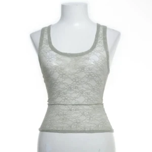 Ljusgrön spetslinne från Monki - Supersnyggt ljusgrönlinne från Monki i transparent spets med blommigt mönster. Modellen är ärmlös med rundad halsringning och figurnära passform. Perfekt att styla lager på lager eller som statement-piece till jeans eller kjol. Aldrig använd 