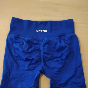 Blå gym shorts från DFYNE - Snygga blå gymshorts från DFYNE med hög midja och ribbad linning. Materialet är stretchigt och passar perfekt för träning. Bakdelen har rynkade sömmar för extra form. Logga framtill och på sidan av linningen.