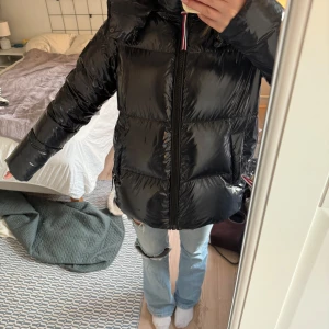 Svart pufferjacka Tommy Hilfiger S - Snygg väldigt mörkblå pufferjacka från Tommy Hilfiger i glansigt material. Jackan har huva, dragkedja framtill och två stora fickor. Perfekt för kalla dagar och har en modern, lite oversized passform. Klassisk logga på ärmen och coola detaljer vid dragkedjan. Han några slitningar men inget som märks när man använder jackan💗