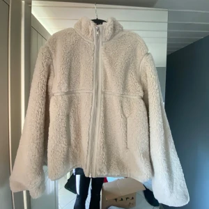 Beige teddyjacka med dragkedja - Mysig beige teddyjacka med hel dragkedja framtill och hög krage. Jackan har två fickor på sidorna och är tillverkad i fluffigt teddy-material som håller dig varm och skön. Perfekt för kyliga dagar och en avslappnad stil❤️❤️