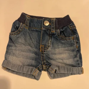 Blå jeansshorts från H&M, stl 50 bebis  - Snygga blå jeansshorts från H&M med mjuk resårmidja och klassiska fickor fram och bak. Shortsen har uppvikta benslut och coola kontrastsömmar. Perfekta för varma dagar och enkel att matcha med allt.