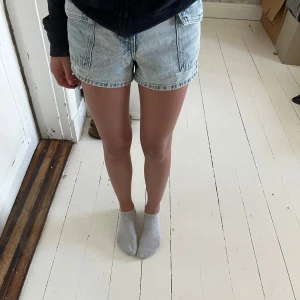 Ljusblå högmidjade jeansshorts - Säljer ett par ljusblå jeansshorts med hög midja och stora fickor framtill. Klassisk femficksmodell med knapp och dragkedja. Perfekta för varma dagar och ger en avslappnad vibe.