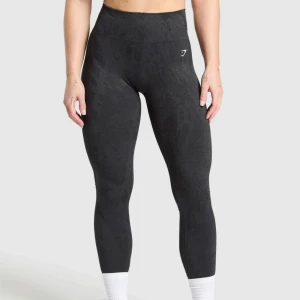 Svarta seamless leggings med scrunch från Gymshark - Svarta seamless leggings från Gymshark med diskret mönster och hög midja. Stretchigt material som sitter tight och bekvämt, perfekt för träning. Liten vit logga på höften. Snygg och sportig look.