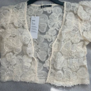 Vit blommig puffärm blus Gina Tricot - Superfin transparent blus från Gina Tricot i vit mesh med stora 3D-blommor över hela tyget. Modellen har korta puffärmar och croppad passform. Perfekt för dig som vill sticka ut med en unik och romantisk look.