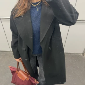 Svart lång kappa från Zara - Säljer min oversize kappa jag har haft i 2 eller 3 vintrar. Välanvänd men har lite noppor (se sista bilden). Inget man tänker på i verkligheten går säkert bort med en noppmaskin.   Material: polyester (men väldigt varm och härlig har använt den i minusgrader) 
