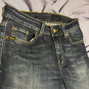 Tiger of Sweden mörkblå jeans - Mörkblå jeans från Tiger of Sweden med snygga slitningar och kontrasterande gula sömmar. Klassisk femficksmodell med smal passform och läderpatch bak i midjan. Perfekta för dig som gillar stilrena och moderna jeans.